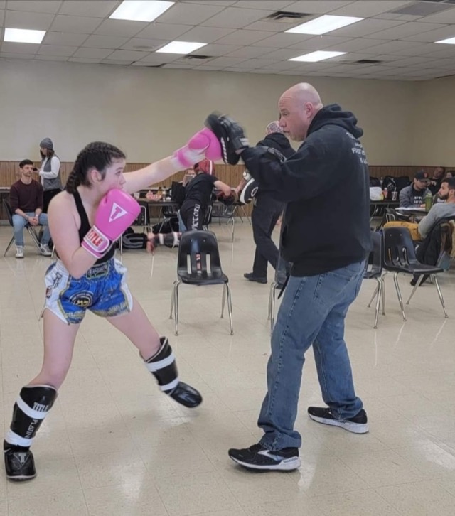 A kickboxer in pink gloves throws a punch at focus mitts held by a coach