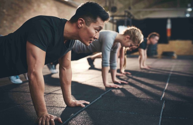 Four people hold a push-up position in a row on the floor during a group fitness class.